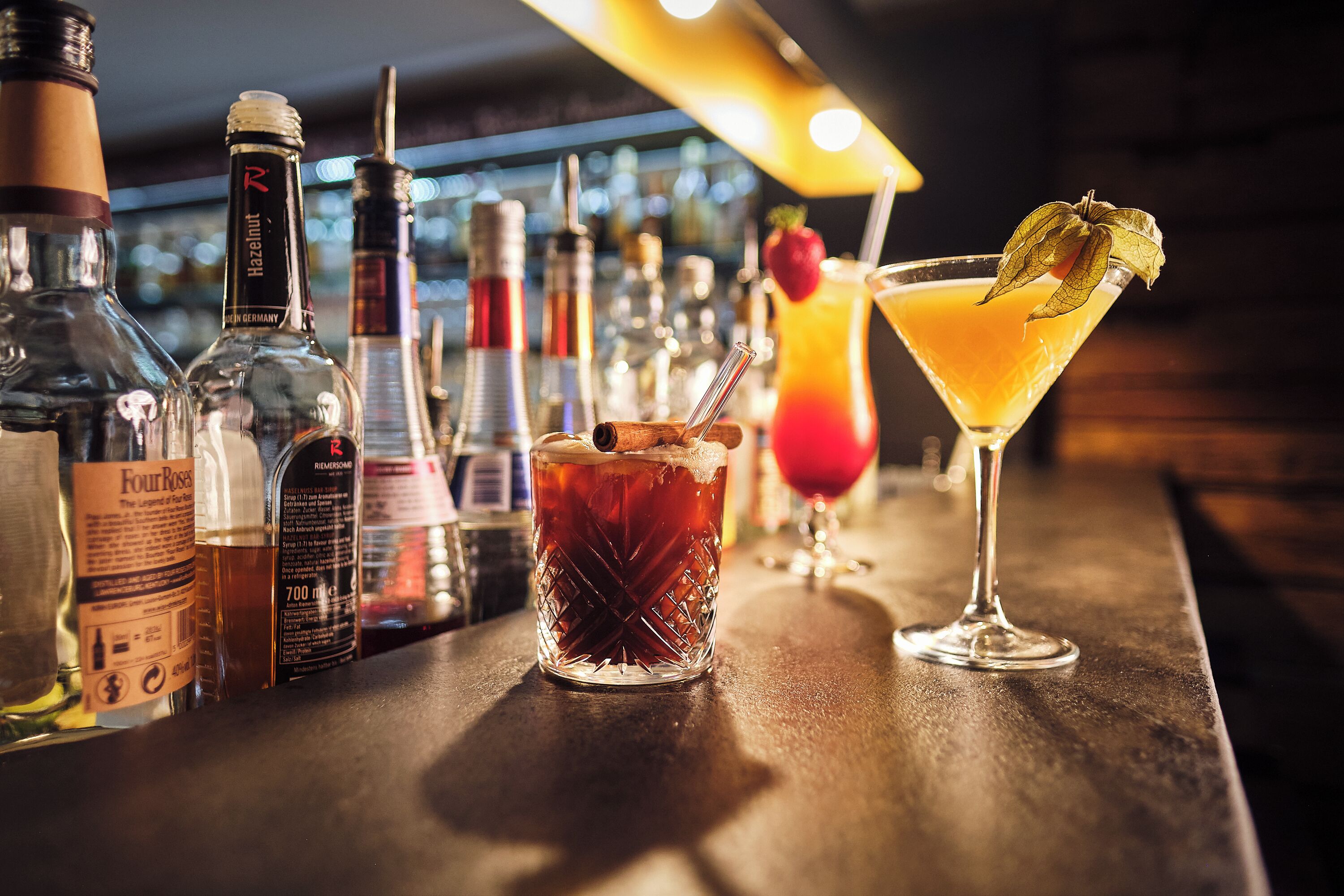A bar with various bottles and two drinks, one with a fruit garnish.