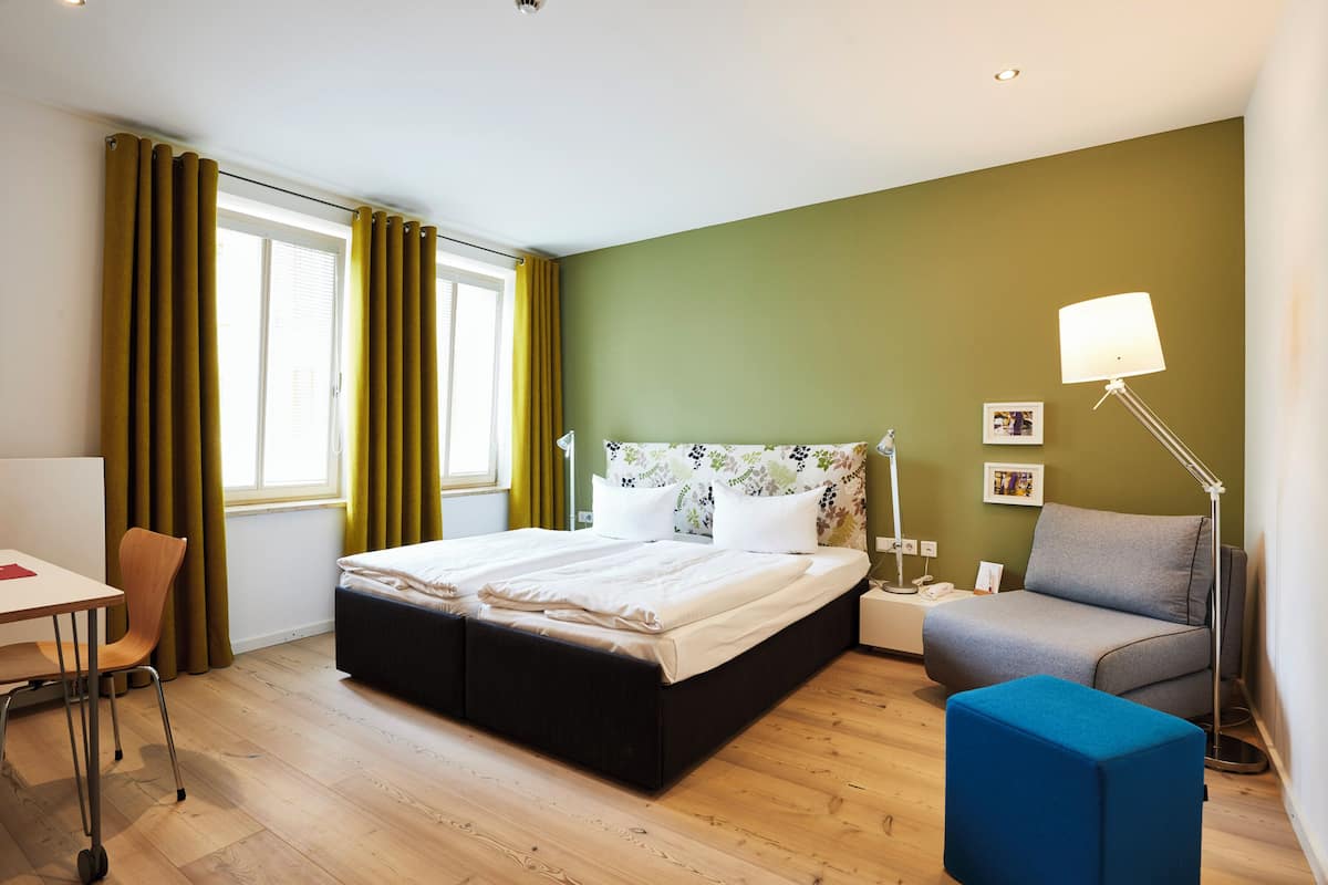 Una habitación de hotel moderna con cama, escritorio, silla, sofá y lámpara.