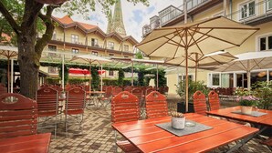 Un café al aire libre con mesas y sillas de madera, sombrillas y un árbol.