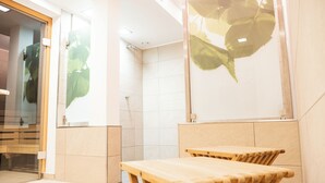 Un baño moderno con cabina de ducha de vidrio, bancos de madera y un mural grande con una hoja verde en la pared.
