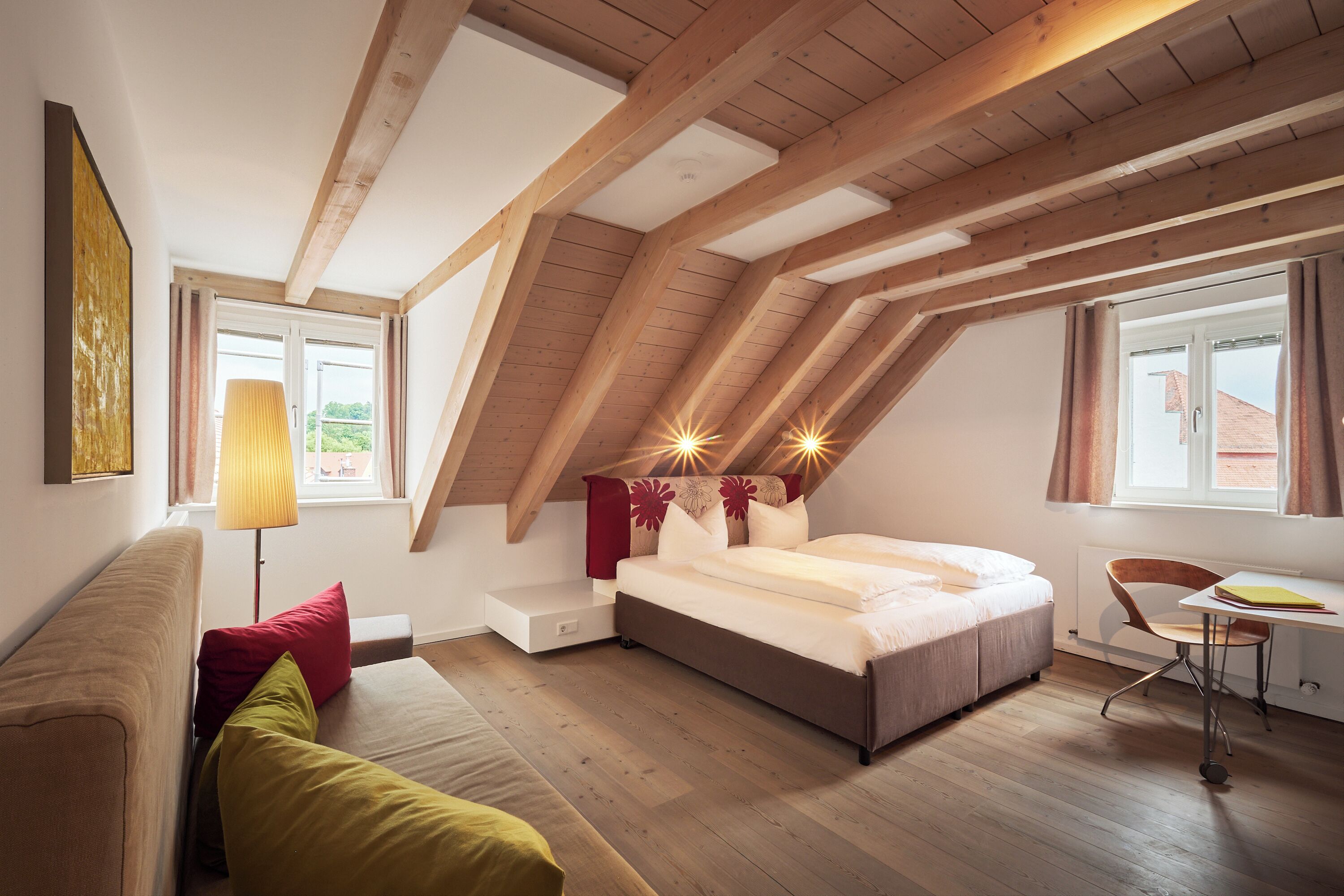 A bedroom with a loft-style ceiling, a bed, a desk, and a chair.