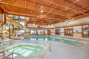 An indoor swimming pool with a hot tub, lounge chairs, and a water slide.