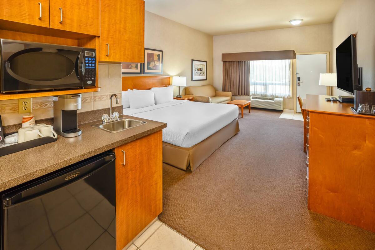 Une chambre d’hôtel équipée d’une kitchenette, d’un lit, d’un canapé, d’une télévision et d’une fenêtre avec des rideaux.