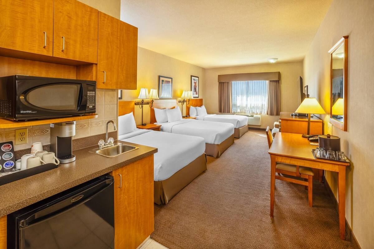 Une chambre d’hôtel avec une kitchenette, deux lits, une table à manger et un grand miroir.