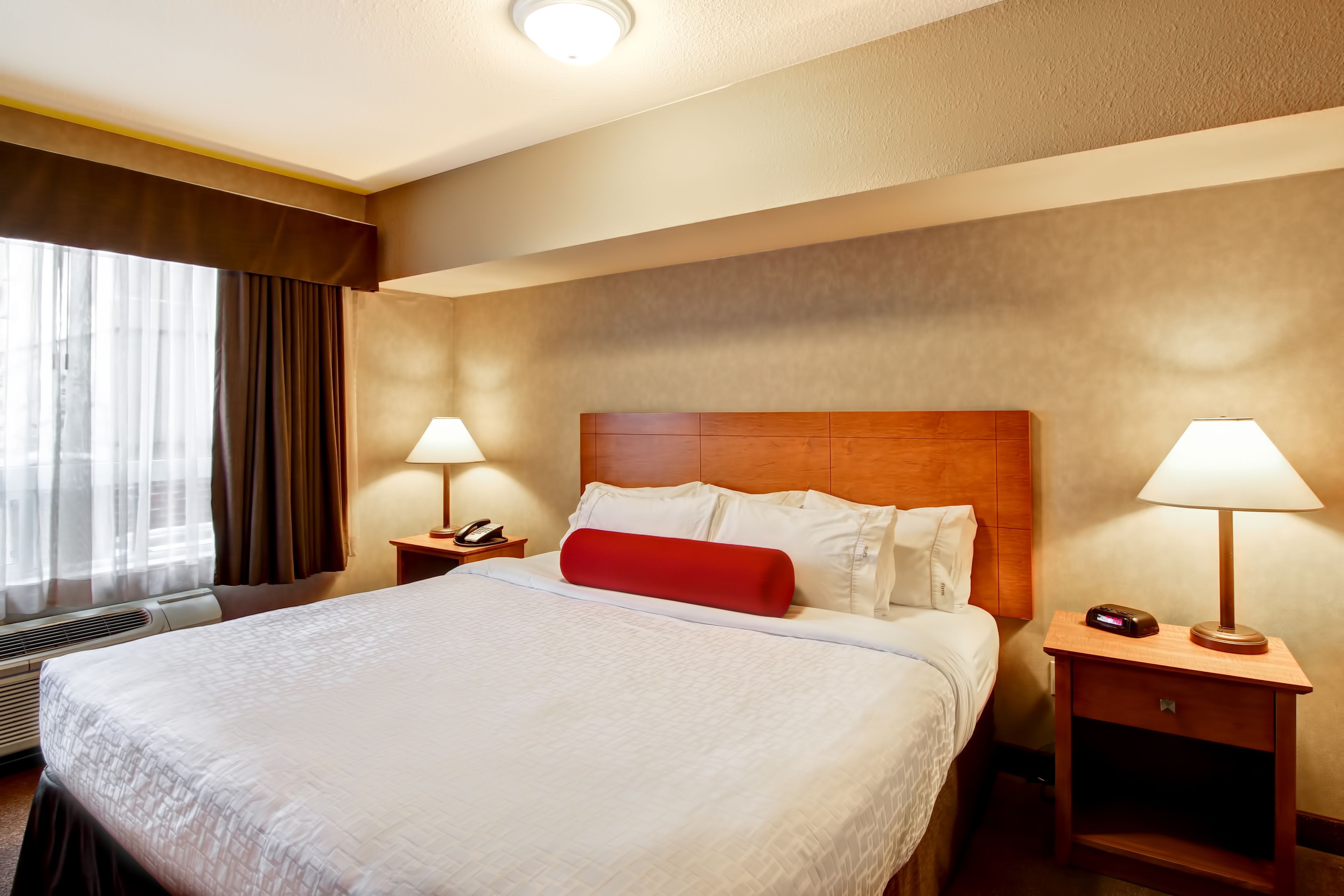 Une chambre d’hôtel avec un grand lit, deux tables de chevet avec des lampes, un oreiller rouge et un téléphone.