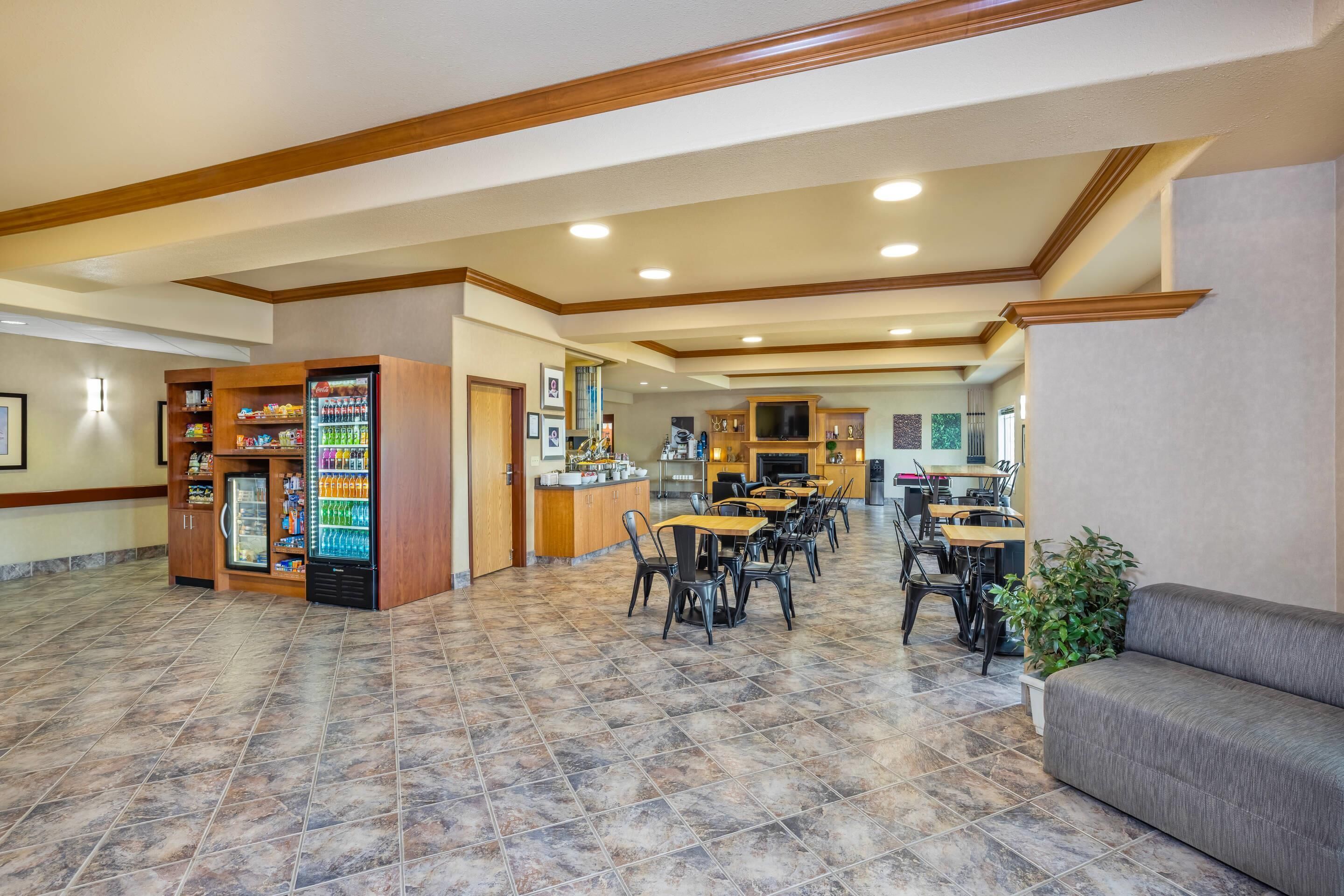 A spacious lobby with a vending machine, a seating area with tables and chairs, and a kitchen in the background.