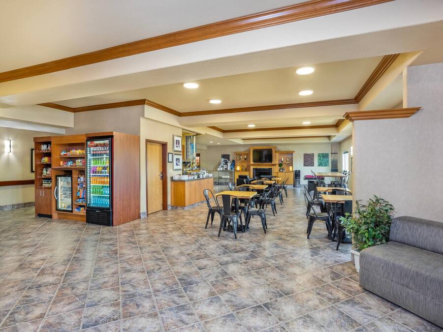 A spacious lobby with a vending machine, a seating area with tables and chairs, and a kitchen in the background.