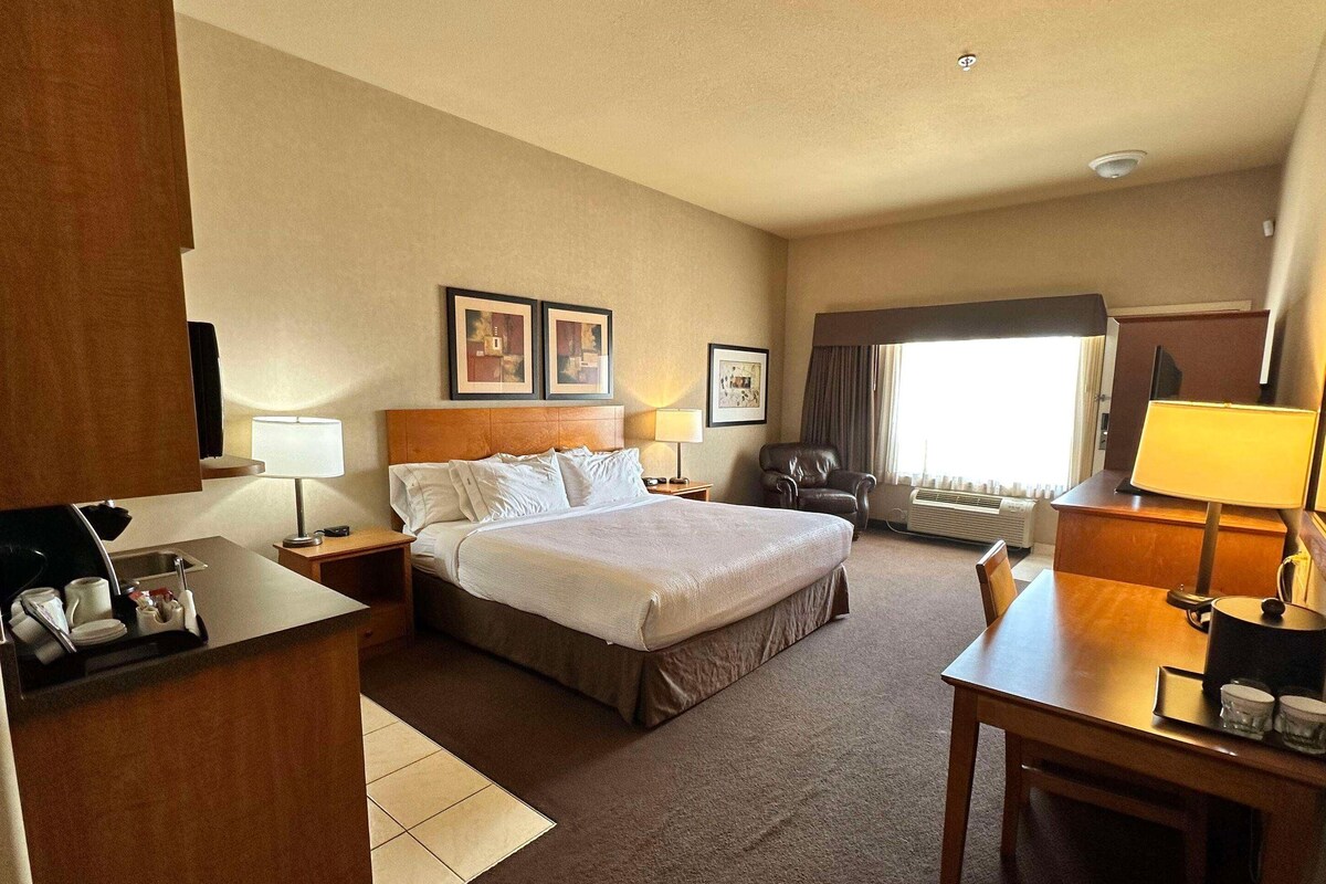 A hotel room with a bed, desk, chair, and a window with curtains.