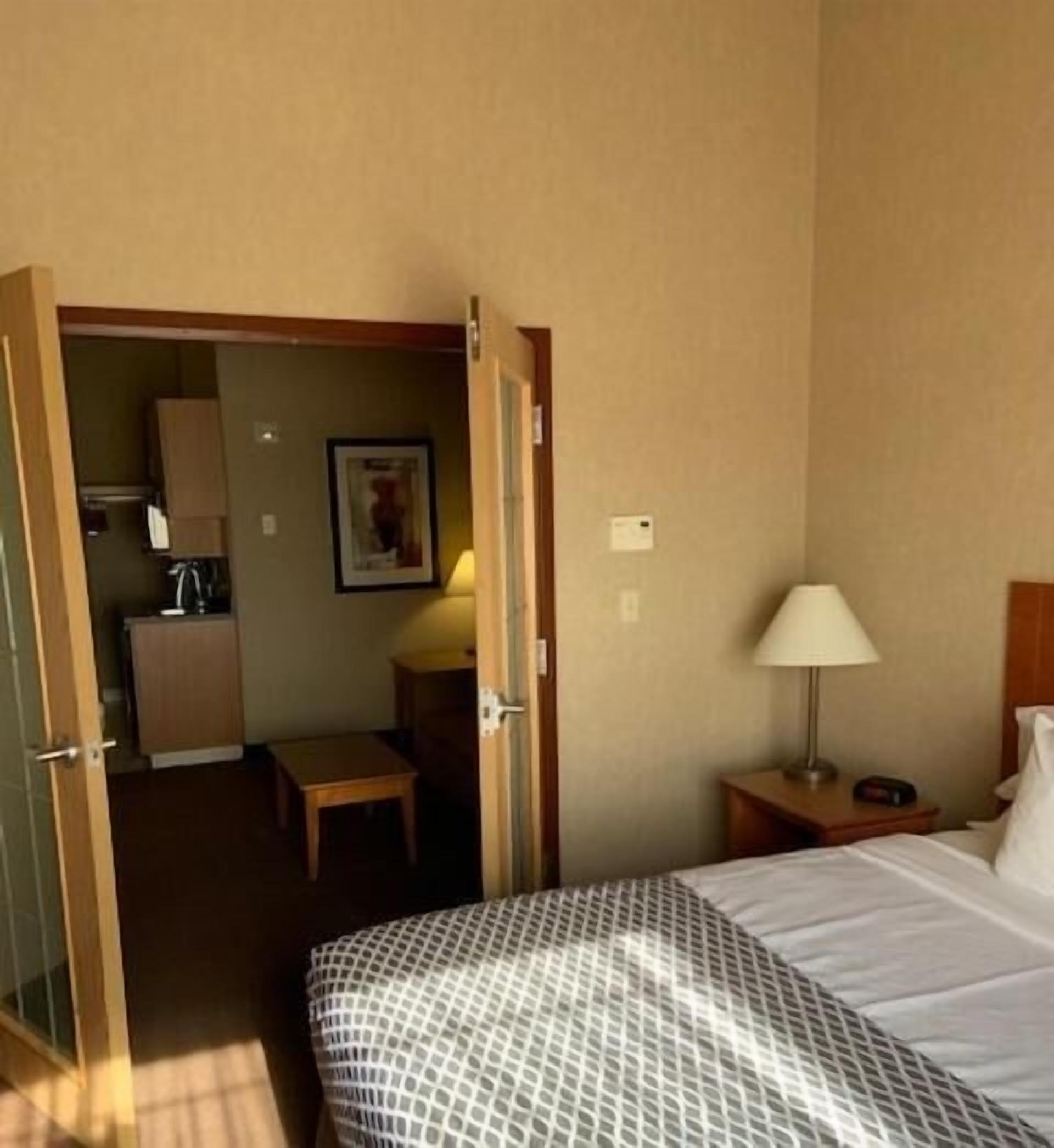 Une chambre d’hôtel comprenant un lit, une table de chevet, une lampe, une petite table et un coin cuisine.