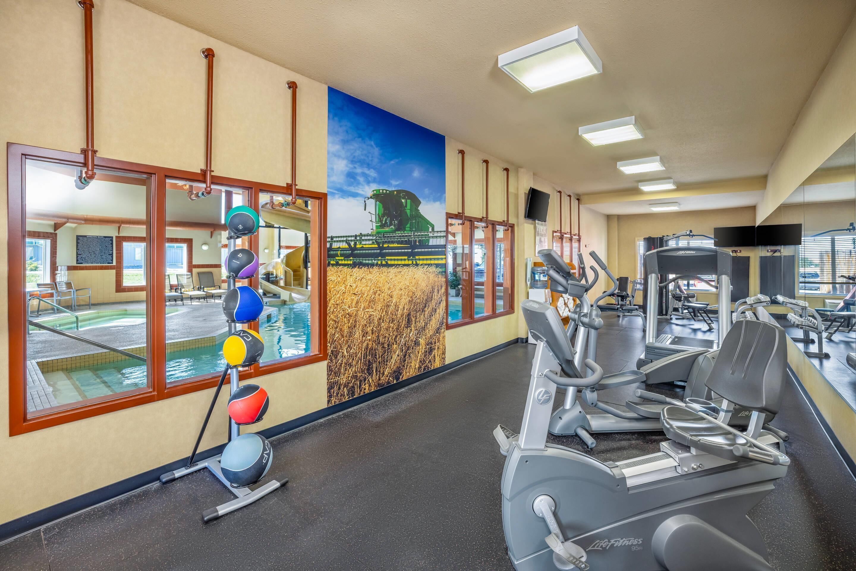 A gym with exercise equipment, a large window, and a mural of a combine harvester.