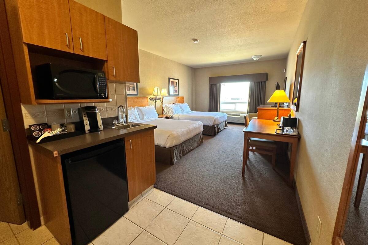 Une chambre d’hôtel avec une kitchenette, deux lits, un bureau et une fenêtre avec des rideaux.