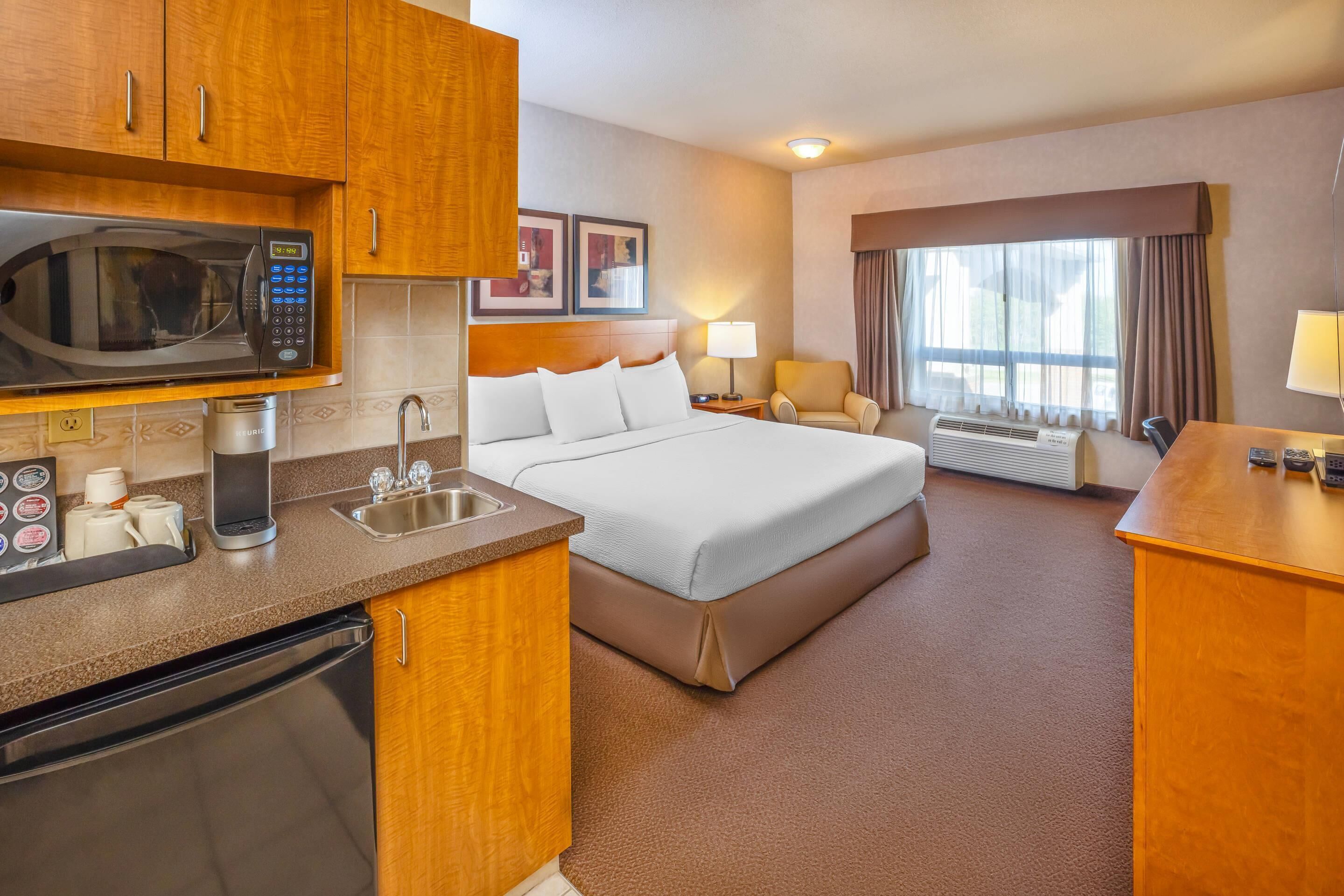 Habitación de hotel con cama, escritorio, microondas, lavamanos, cafetera y ventana con cortinas.