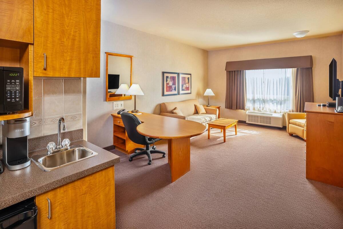 Une chambre d’hôtel équipée d’une kitchenette, d’un coin repas, d’un canapé, d’une télévision et d’une grande fenêtre.