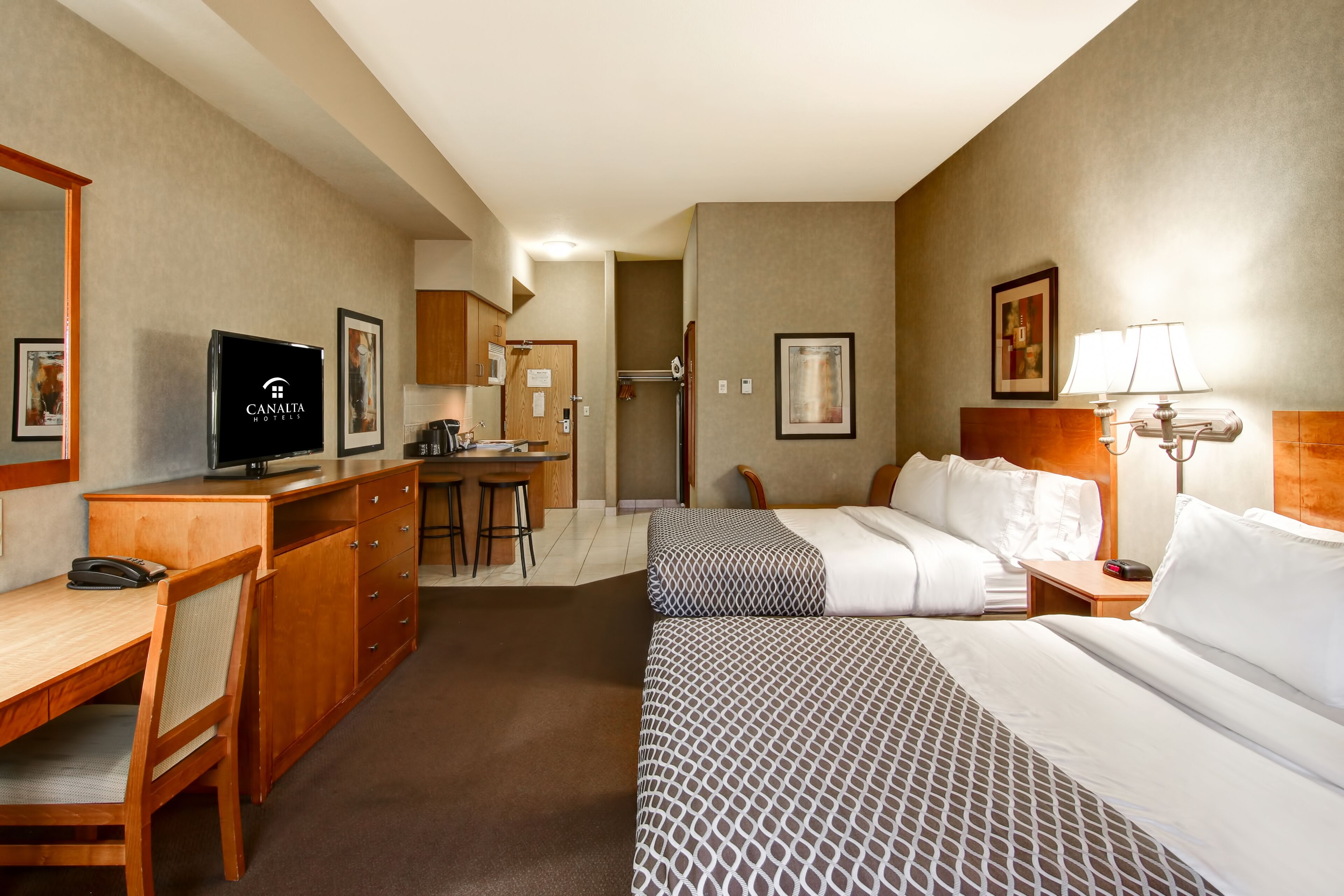 A hotel room with a bed, desk, and kitchenette.