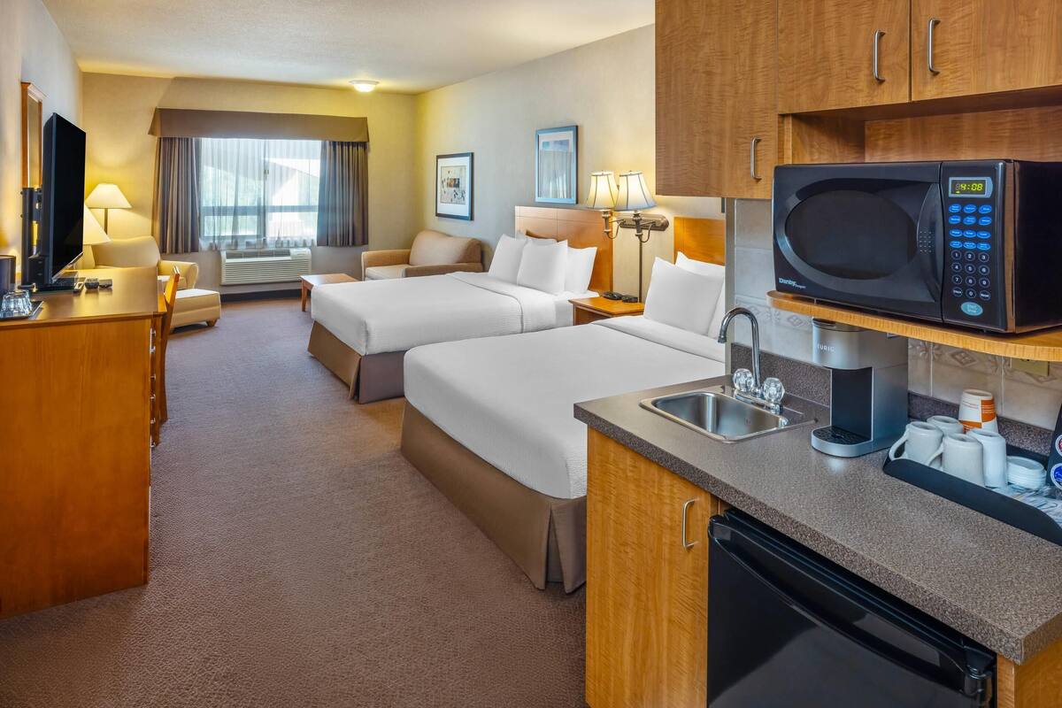 Une chambre d’hôtel avec deux lits, un bureau, une télévision, un four à micro-ondes, un lavabo et une fenêtre avec des rideaux.