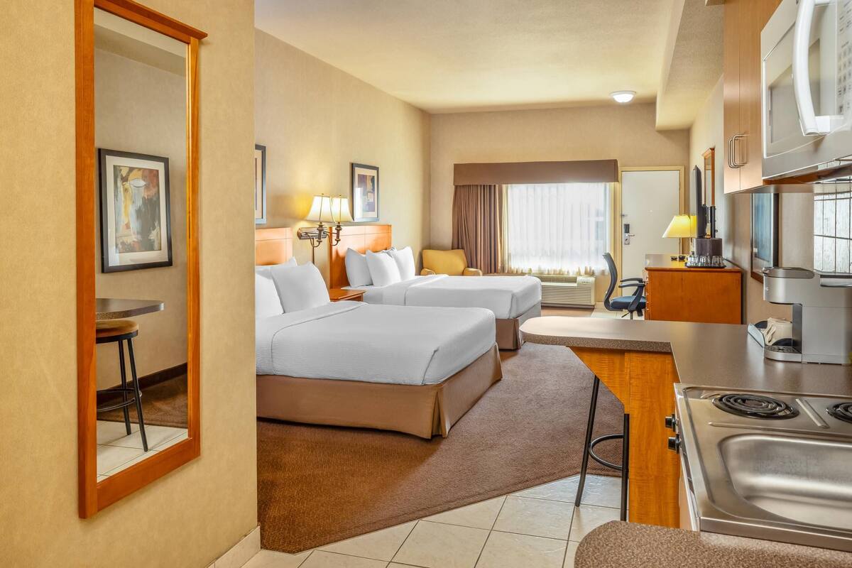 Une chambre d’hôtel avec deux lits, une kitchenette, un coin repas et une salle de bain visible à travers une porte ouverte.