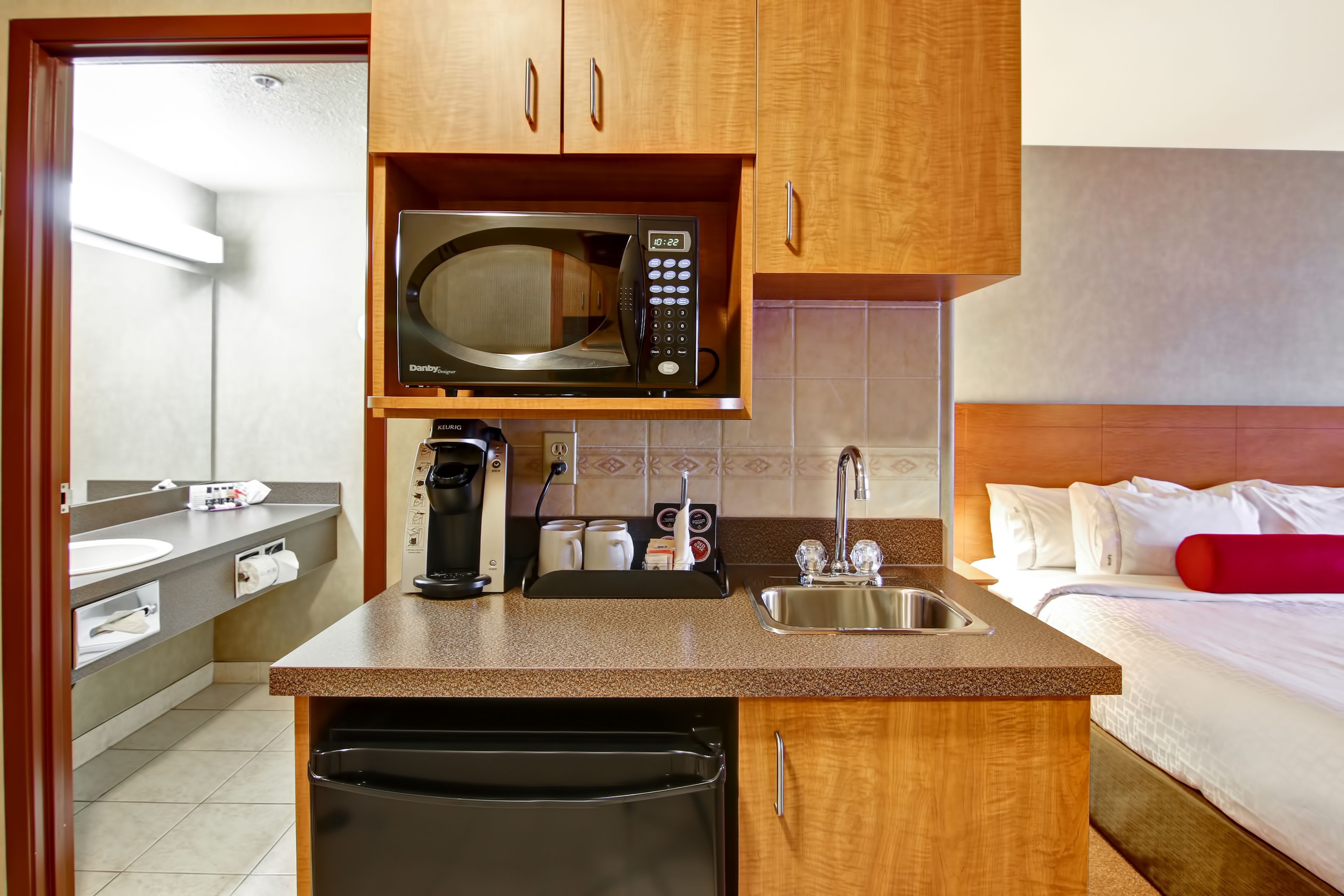 A compact hotel room with a kitchenette, including a microwave, coffee maker, and sink.