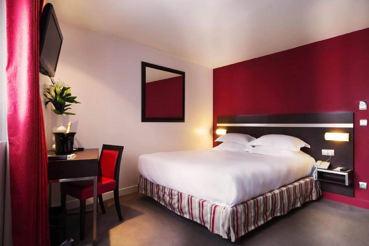 A hotel room with a bed, a desk with a chair, a TV mounted on the wall, and a mirror.