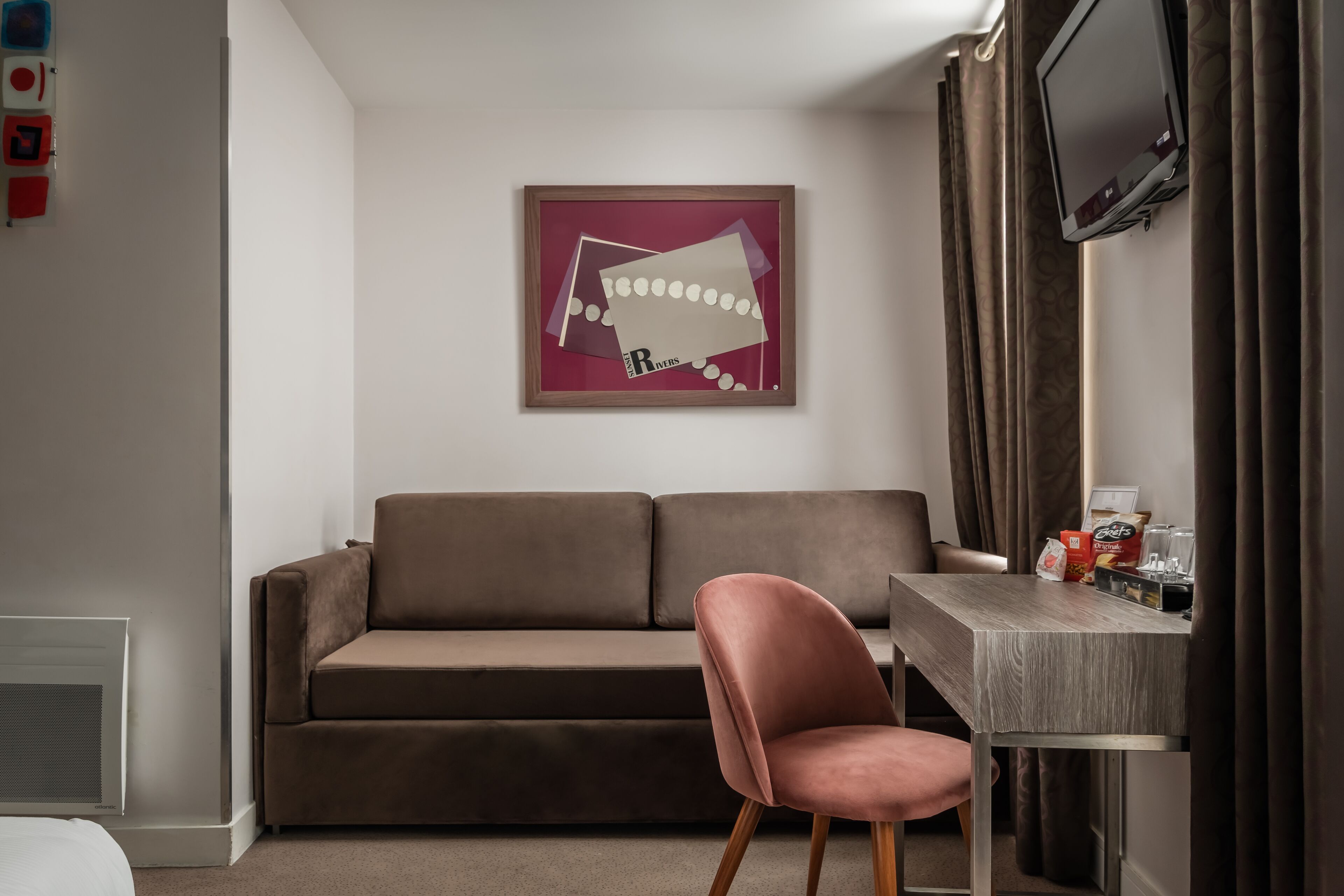 A modern room with a brown sofa, a pink chair, a wooden desk, and a television on the wall.