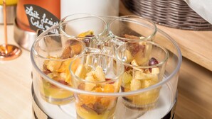 A glass serving dish with fruit and a drink, a white pitcher, and a wicker basket in the background.