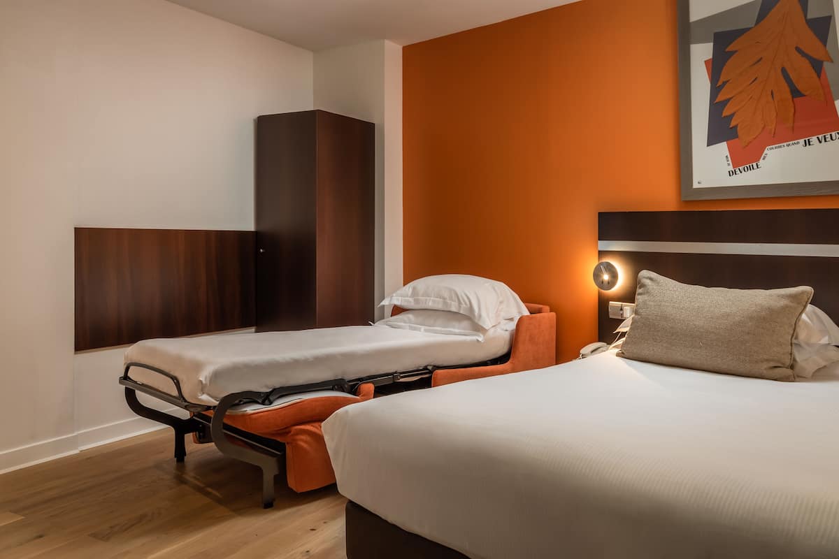 A hotel room with two single beds, a wardrobe, and a large poster on the wall.