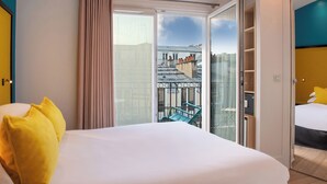 A hotel room with a large bed, a sliding glass door to a balcony, and a view of the cityscape.