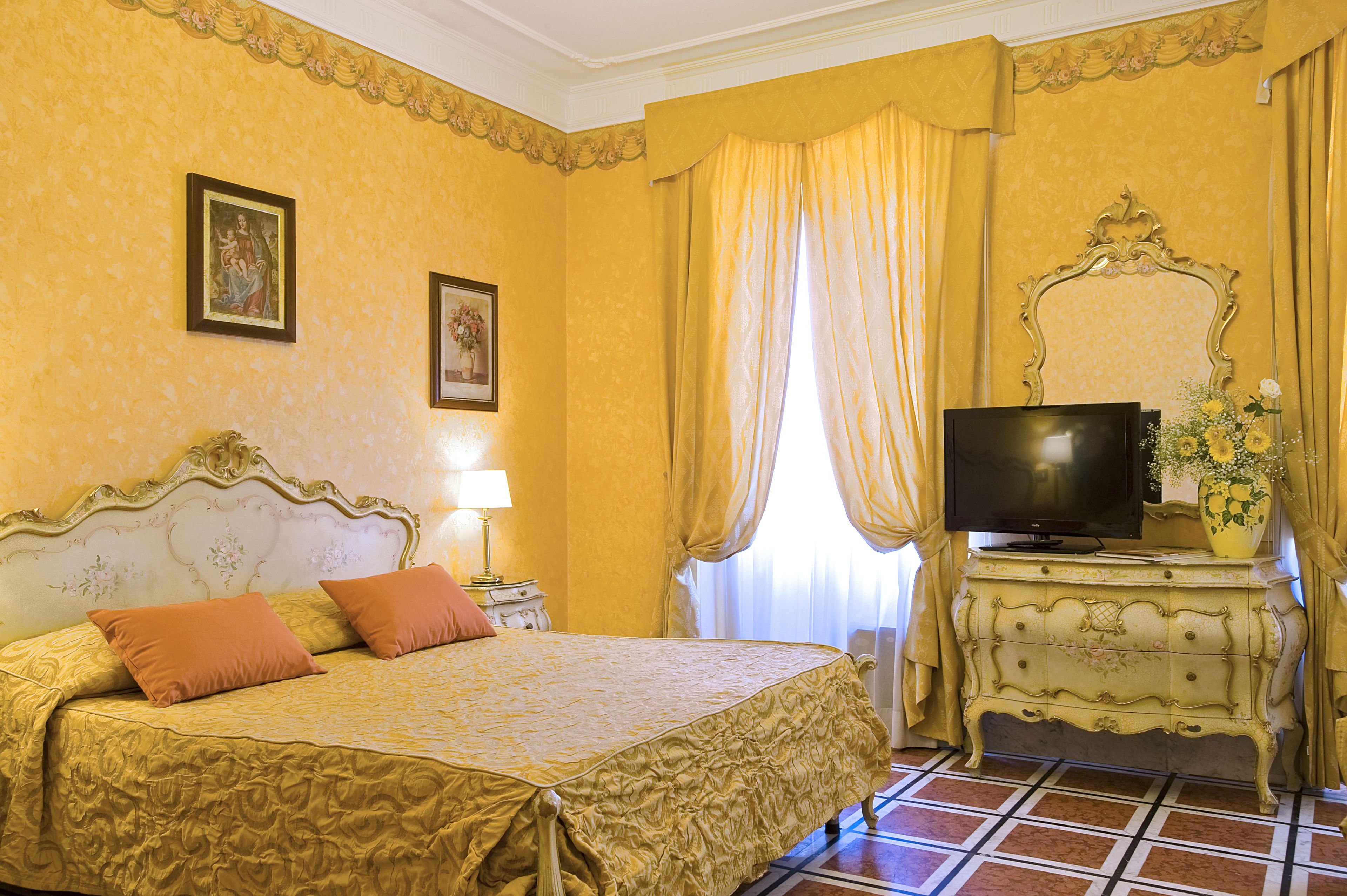 Una habitación de hotel con una cama grande, televisión, cómoda y ventana con cortinas.