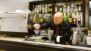 Baarialue, jossa on kahvinkeitin, hyllyt täynnä alkoholijuomapulloja ja baaritarvikkeita.