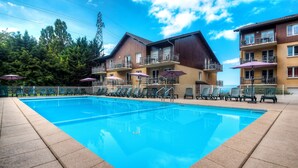 A swimming pool with lounge chairs and umbrellas, surrounded by multi-story buildings with balconies. - Zenitude Evian Les Terrasses du Lac (Evian-les-Bains)