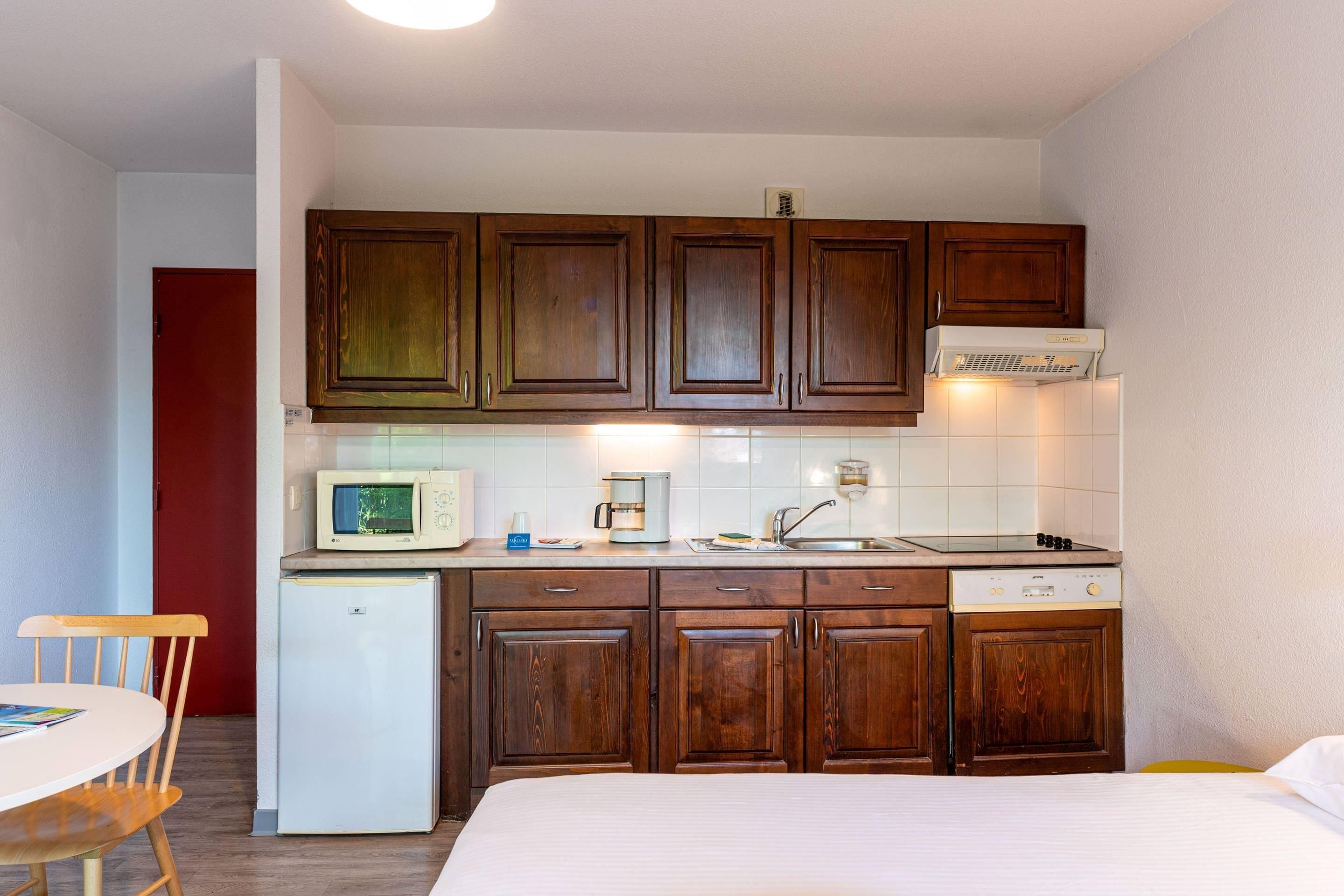 A compact kitchen with wooden cabinets, a microwave, a coffee maker, and a small refrigerator.