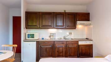 A compact kitchen with wooden cabinets, a microwave, a coffee maker, and a small refrigerator.