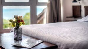 A bed with a view of the outdoors, a bedside table with a vase of flowers, and a lamp on the wall. - Zenitude Evian Les Terrasses du Lac (Evian-les-Bains)