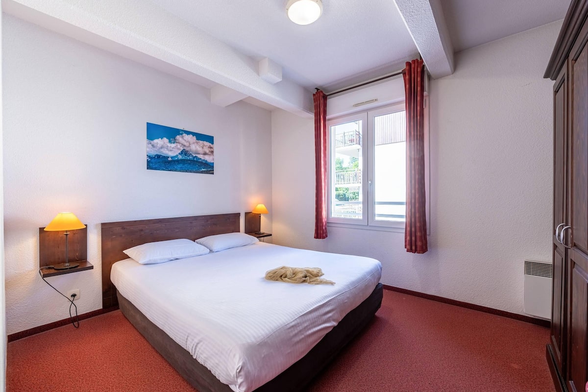 A neatly made bed with white linens, a wooden headboard, and a painting of a seascape on the wall.