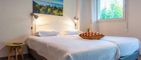 A double bed with white bedding, a bedside table with a lamp, and a window with a view of trees.