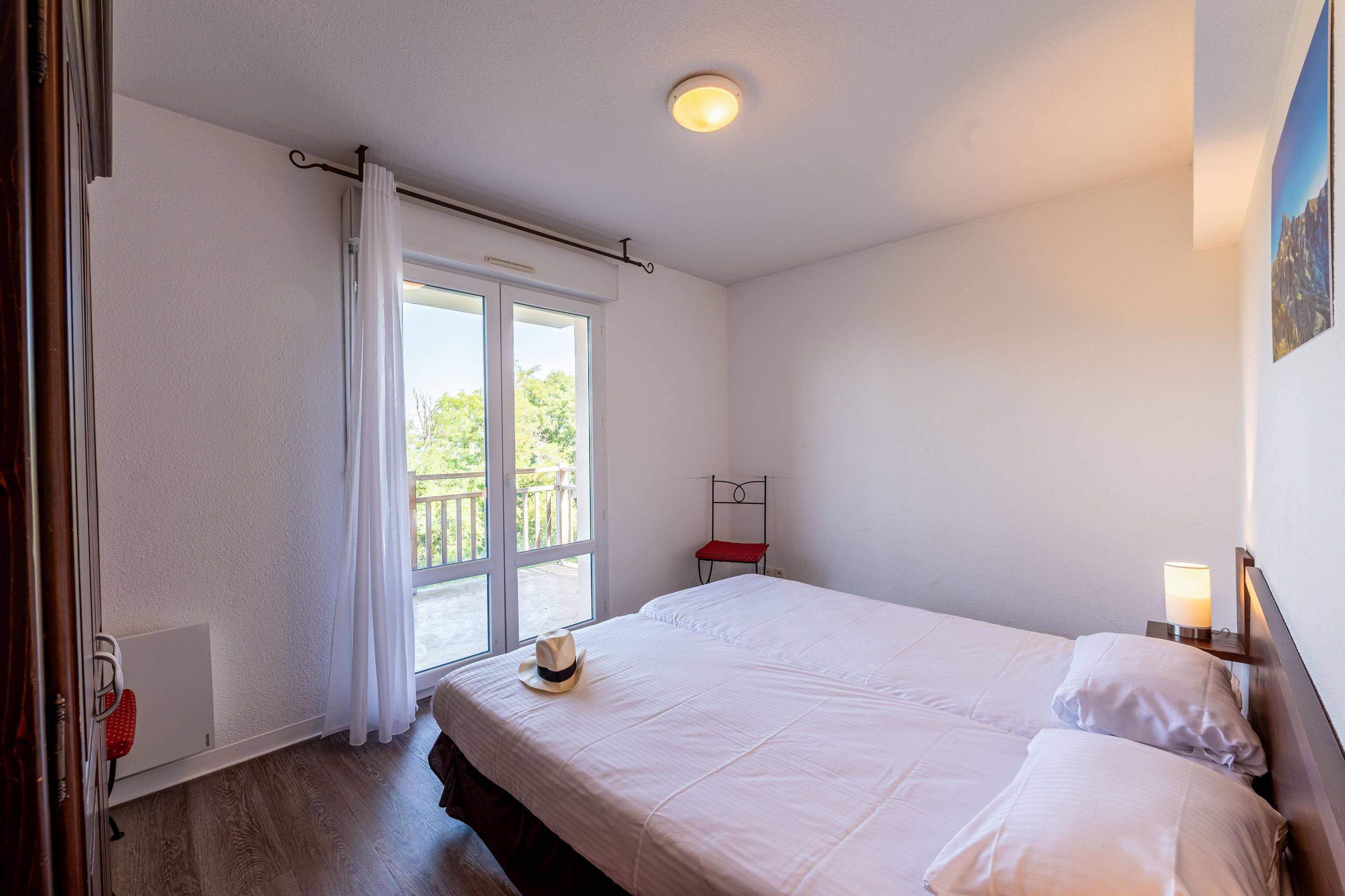 Una camera d'albergo con un letto, una finestra con tende, un comodino con una lampada e vista sull'esterno.