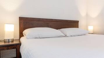A neatly made bed with white linens and two bedside lamps on wooden nightstands.