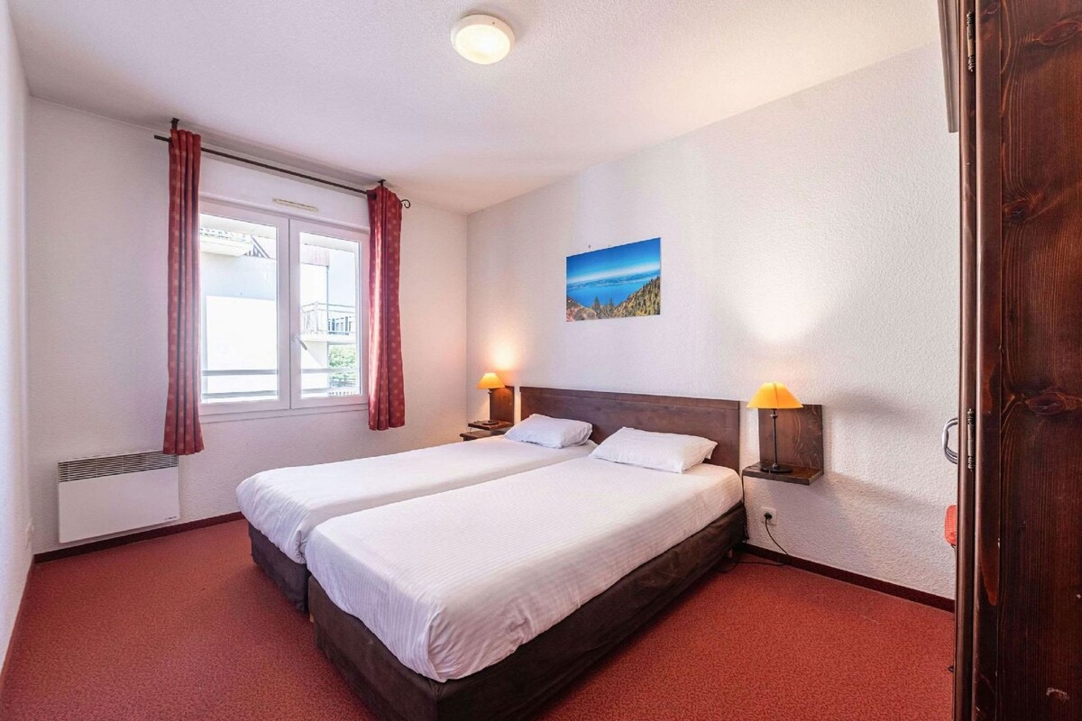 A hotel room with two beds, a window with curtains, a wall-mounted picture, and bedside lamps.