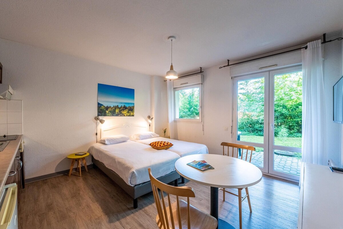 A modern bedroom with a bed, bedside table, and a view of greenery through a sliding glass door.
