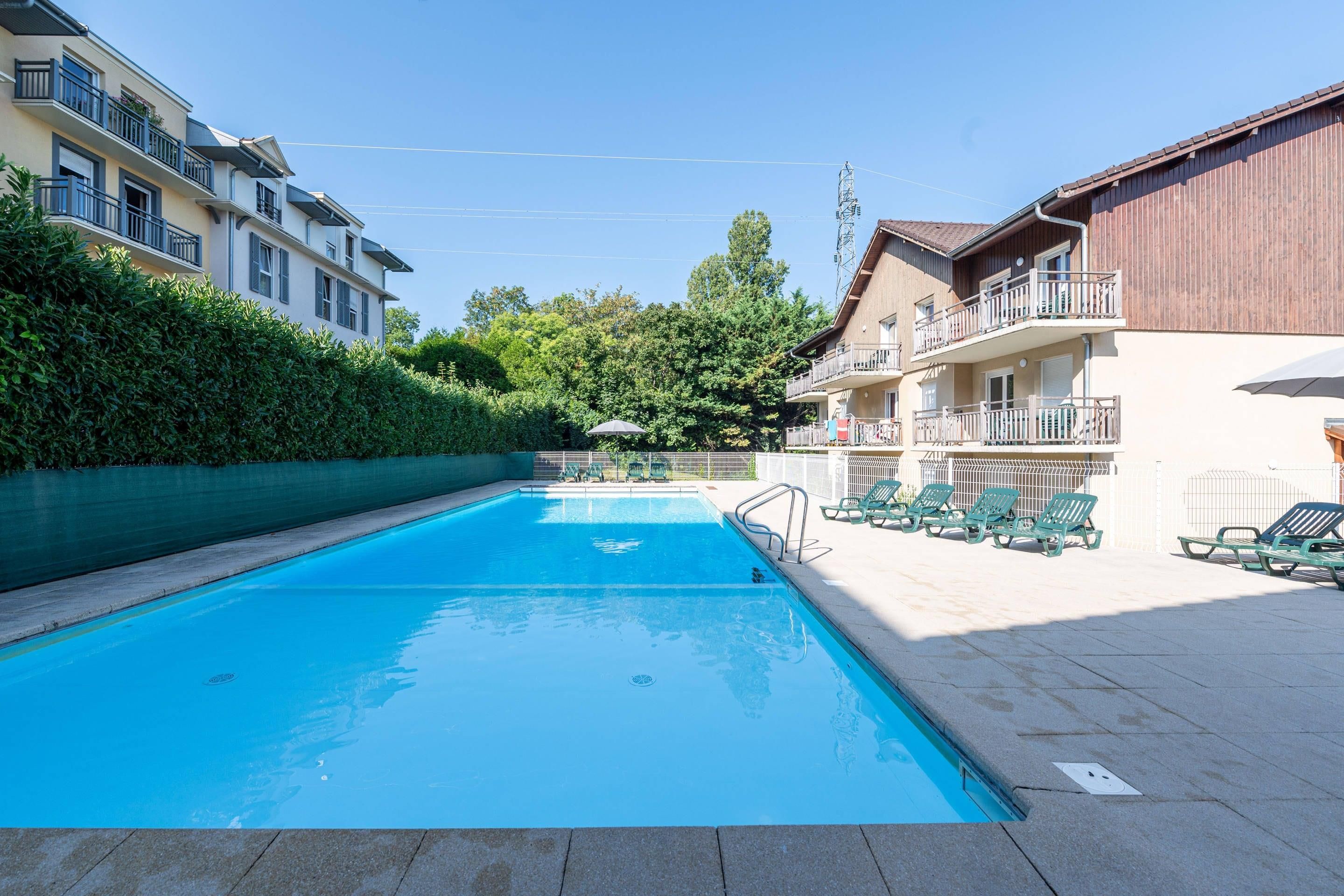 A swimming pool with lounge chairs and a hedge.