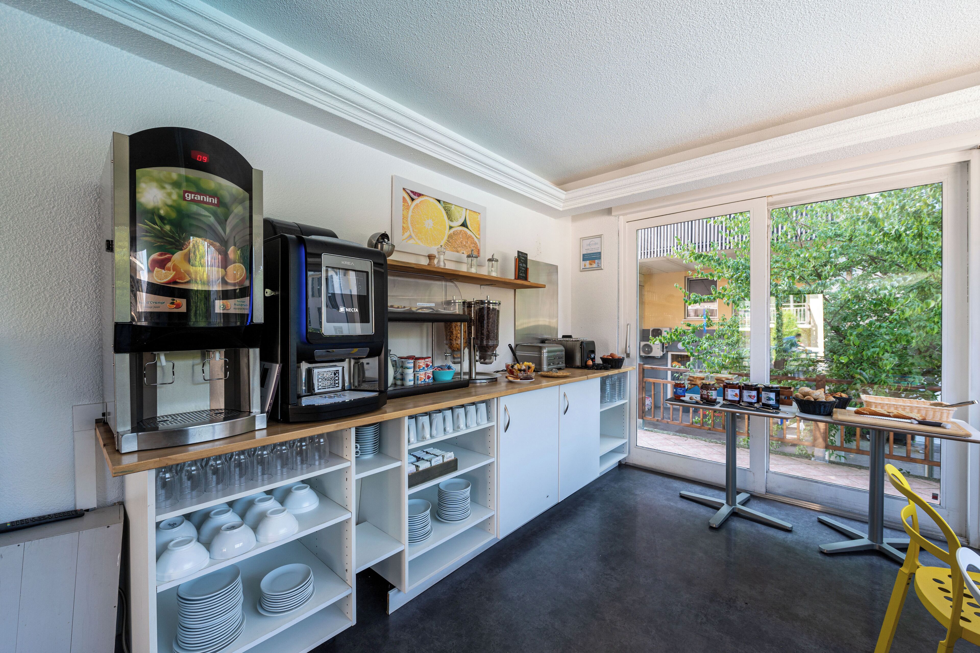A breakfast bar with coffee machines, a fruit display, and a view of the outdoors.