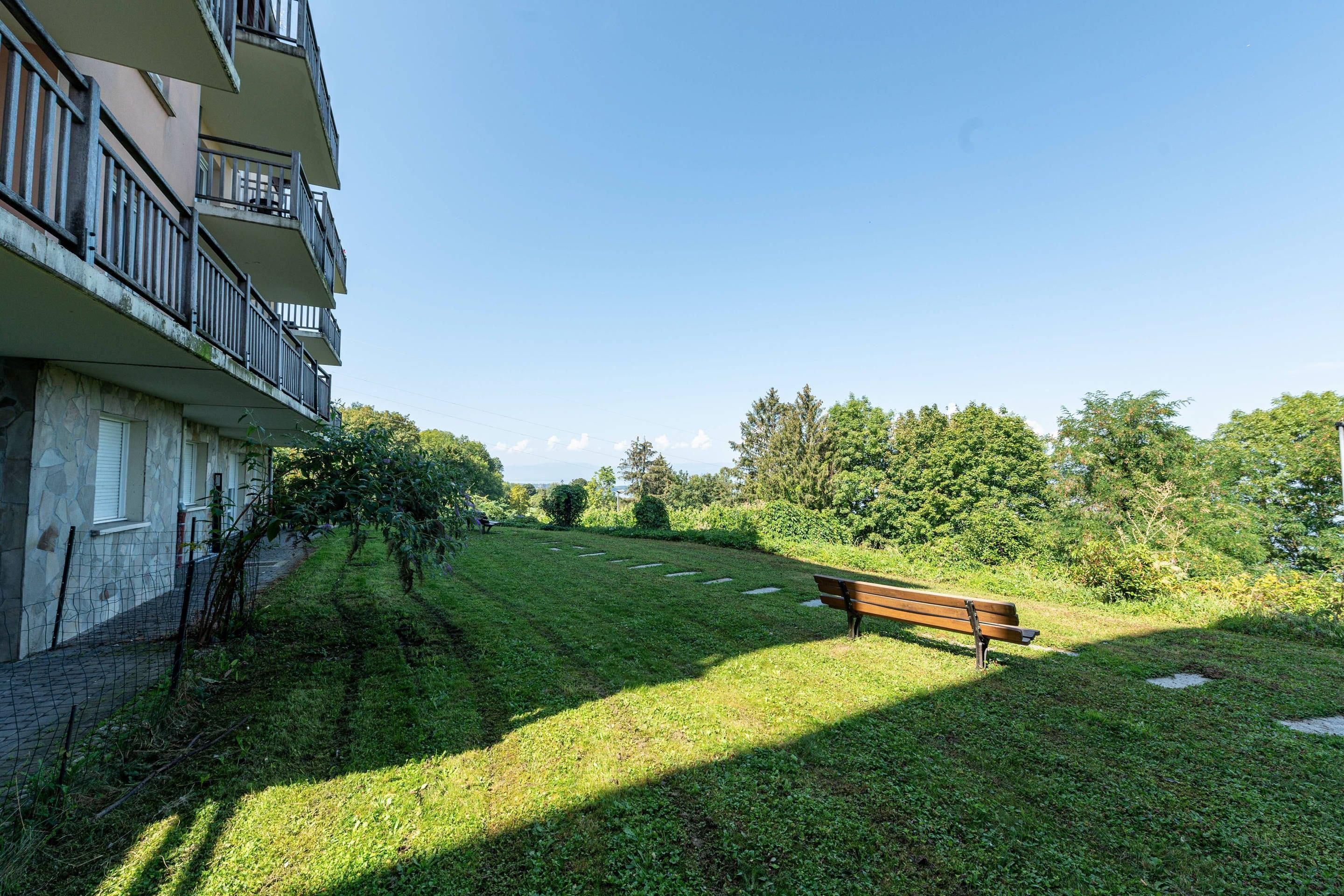 Un espace verdoyant avec un banc, un mur de pierre et un bâtiment doté de balcons.