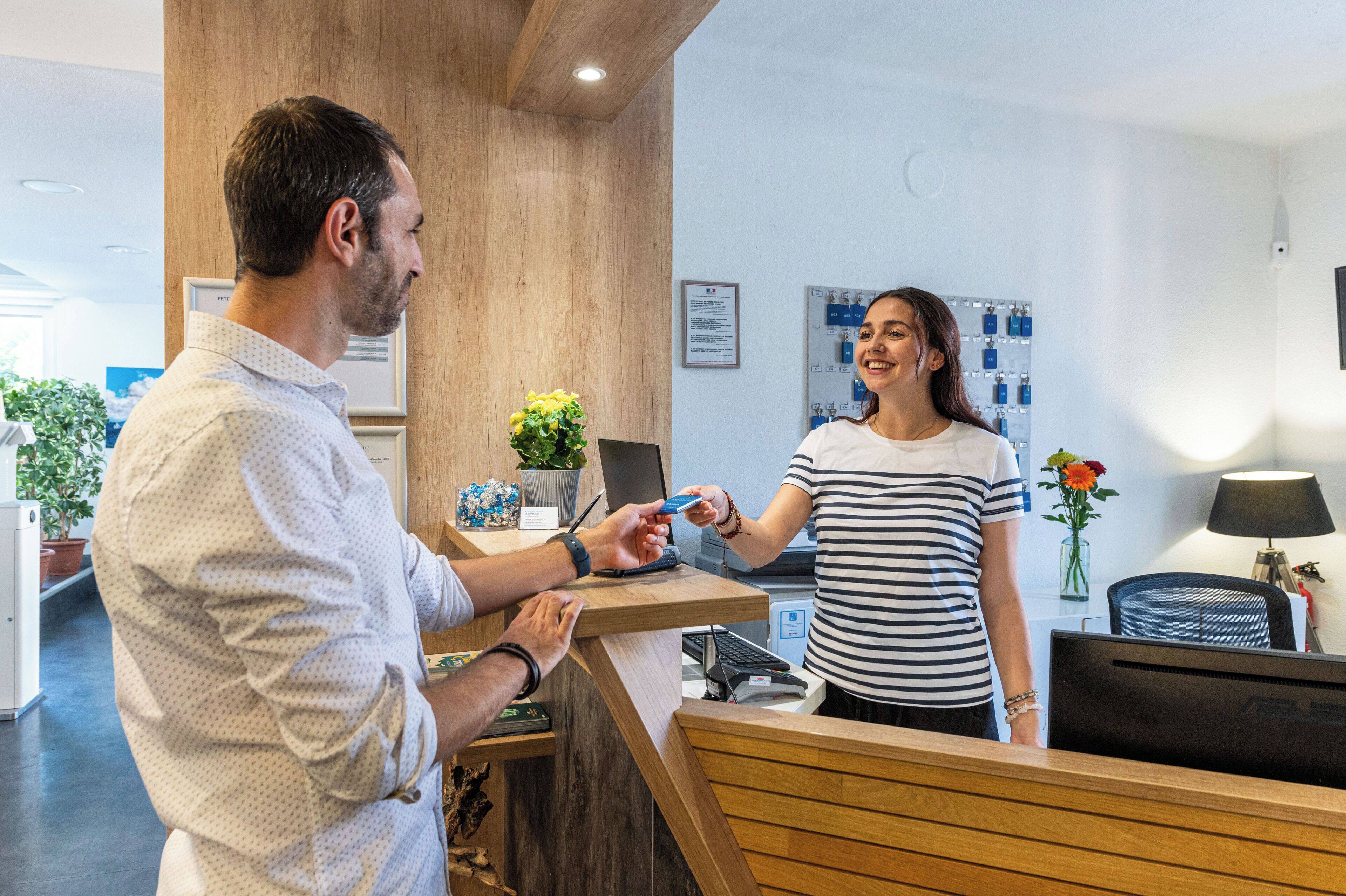 Un mostrador de recepción con encimera de madera, un monitor de computadora y una planta en maceta.