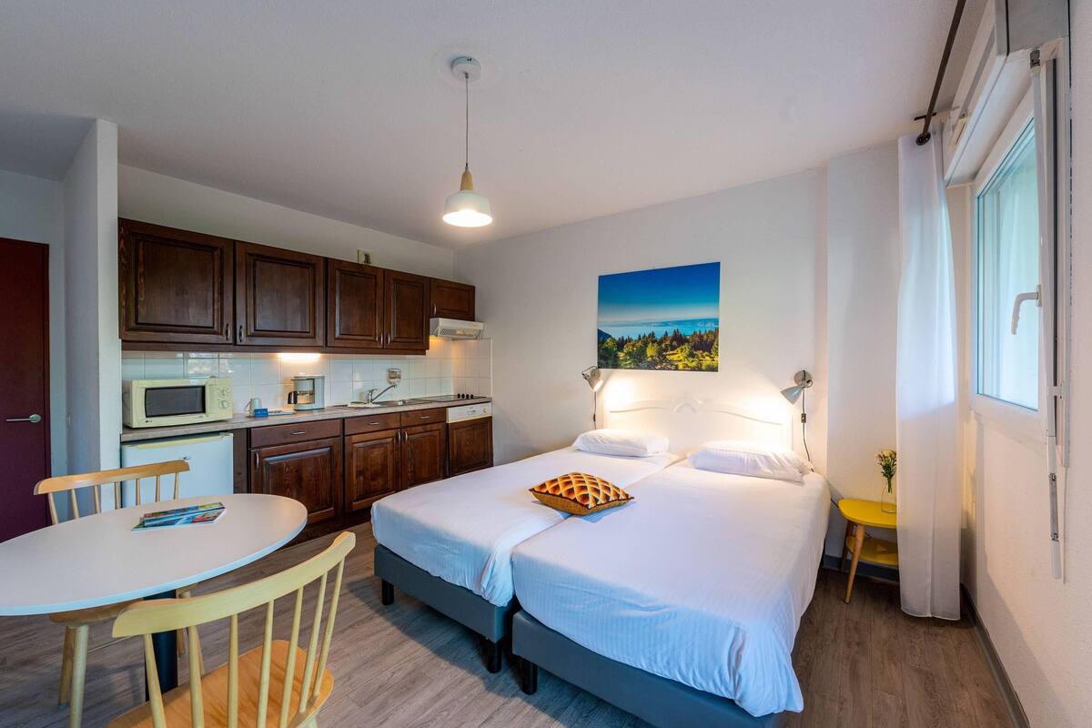 A compact room with a bed, a small table, a chair, a microwave, and a sink.