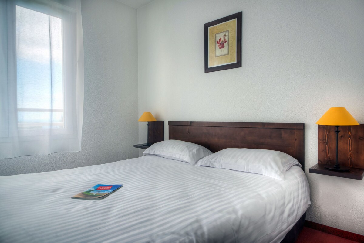 A neatly made bed with white linens, a framed picture on the wall, and two bedside lamps.