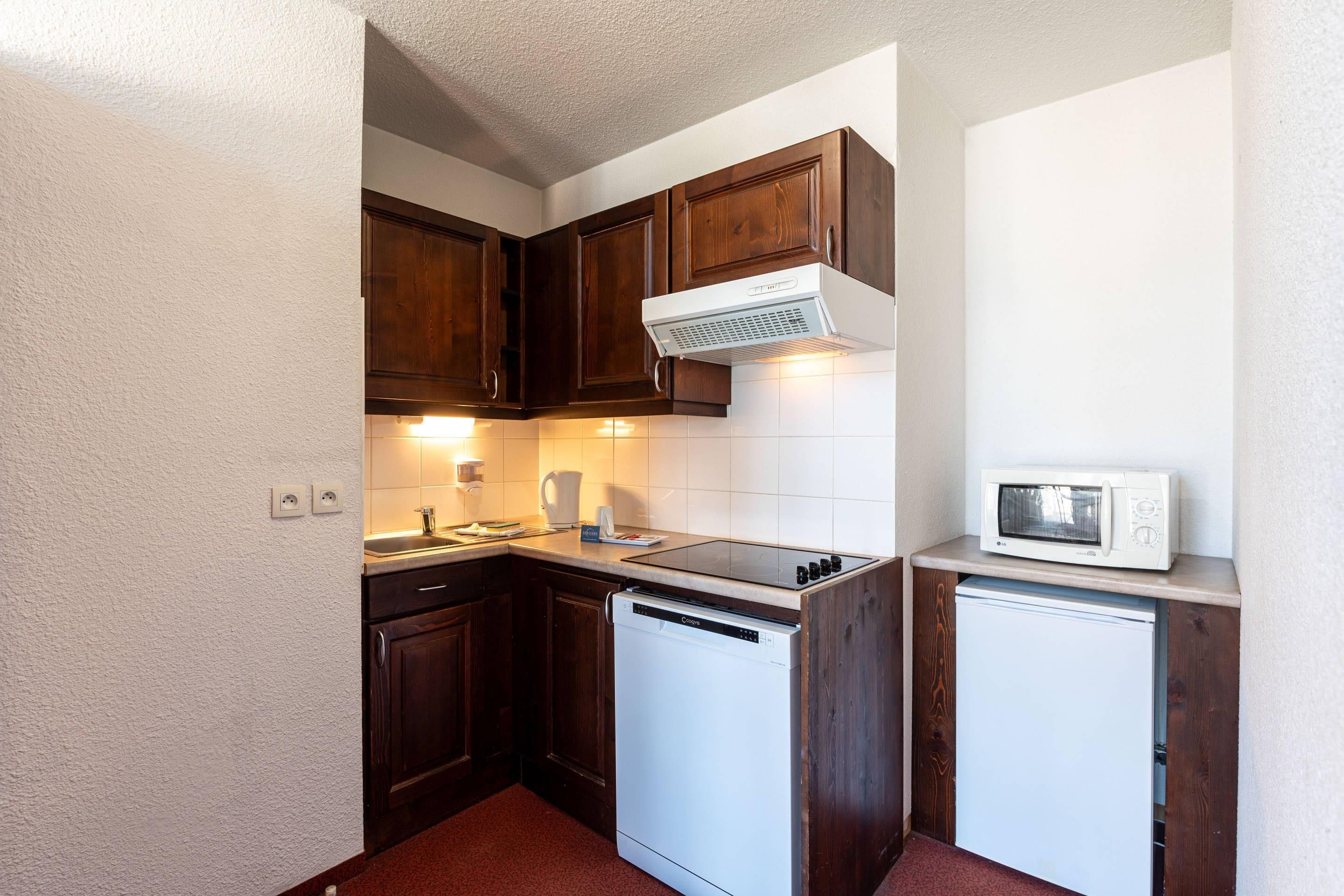 A compact kitchen with wooden cabinets, a dishwasher, a microwave, and a built-in oven.