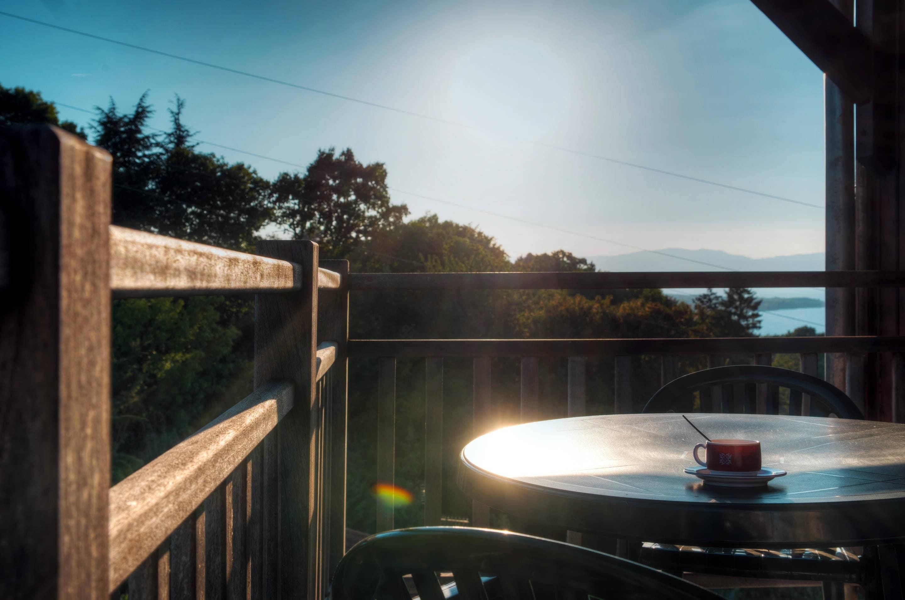 Een balkon met een tafel en een kopje, met uitzicht op een prachtig landschap met bomen en bergen.