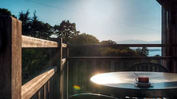 Een balkon met een tafel en een kopje, met uitzicht op een prachtig landschap met bomen en bergen.