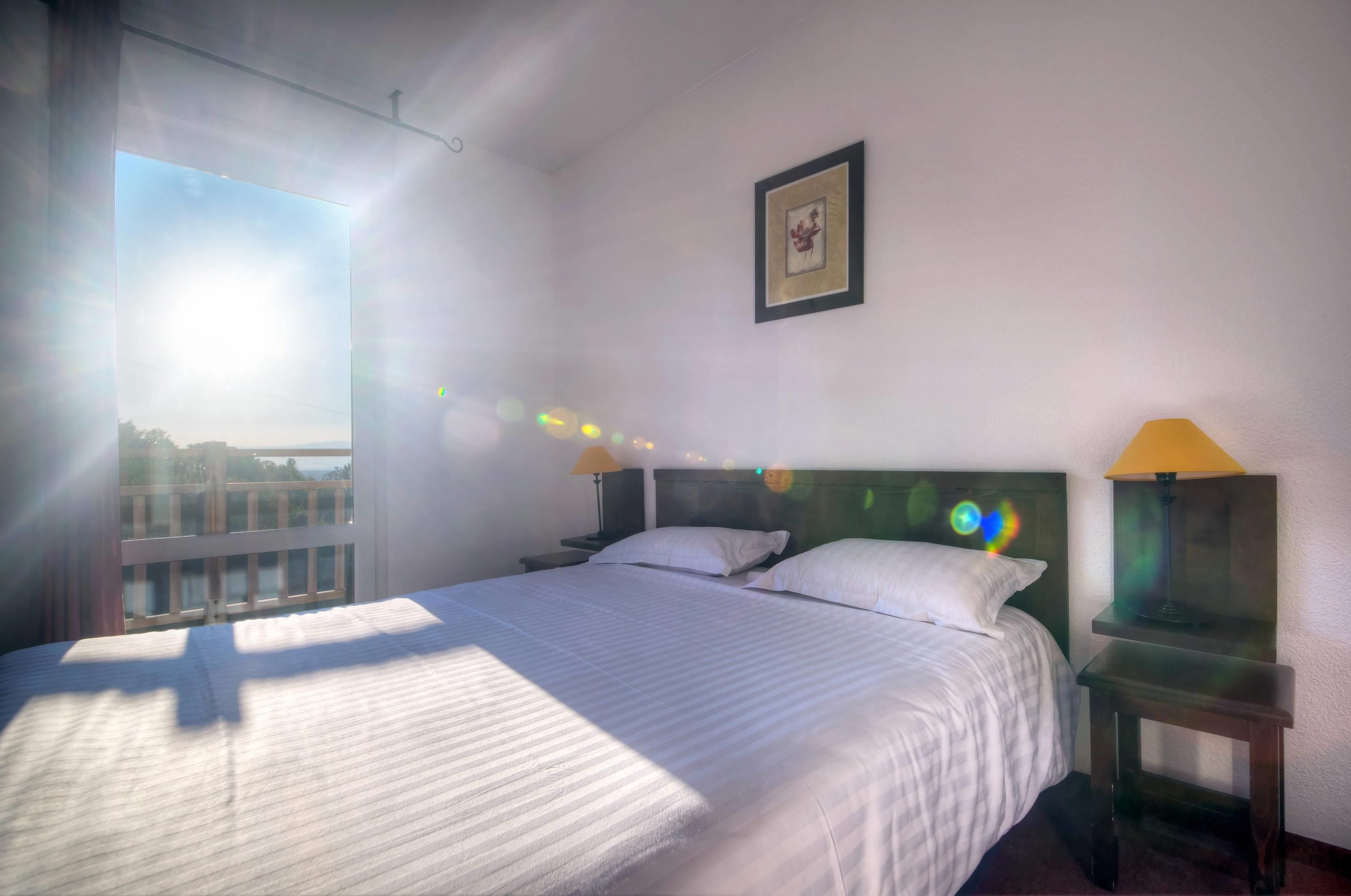 A hotel room with a large bed, two bedside tables with lamps, a framed picture on the wall, and a view of the city through the window.
