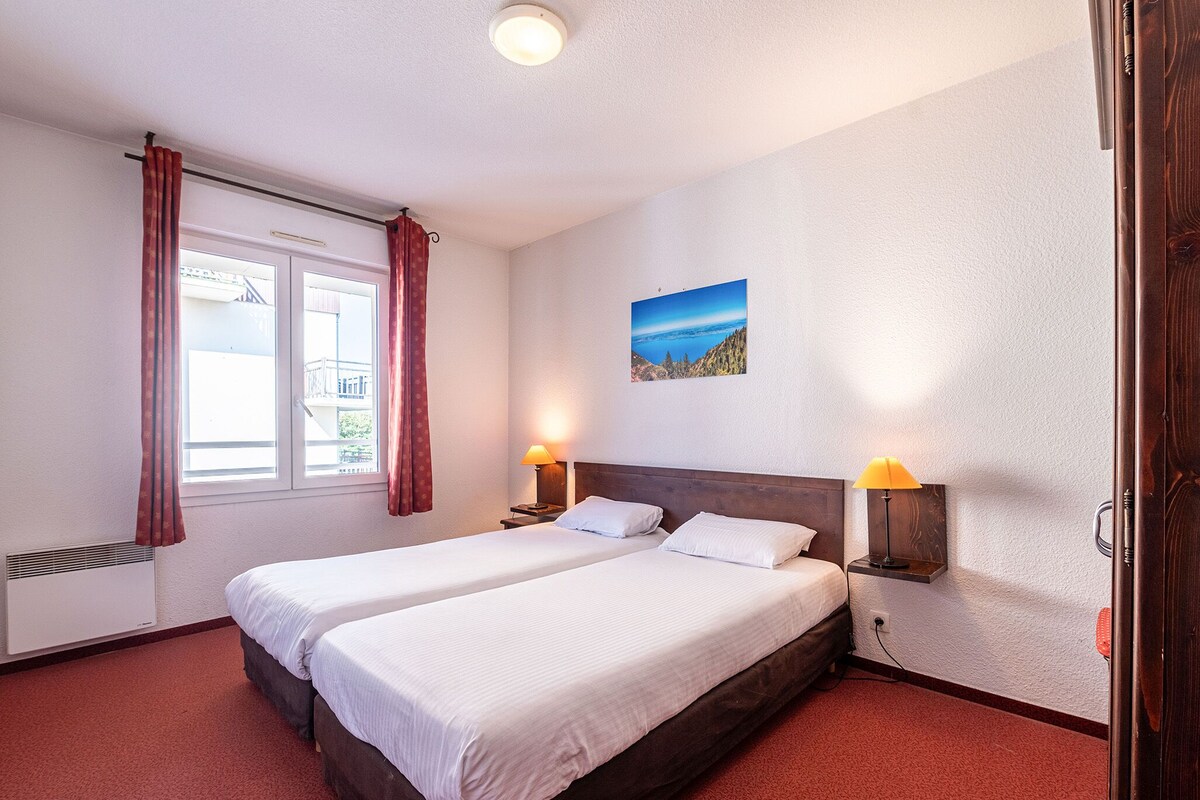 A double bed with two pillows, a window with curtains, a wall-mounted picture, and bedside lamps.