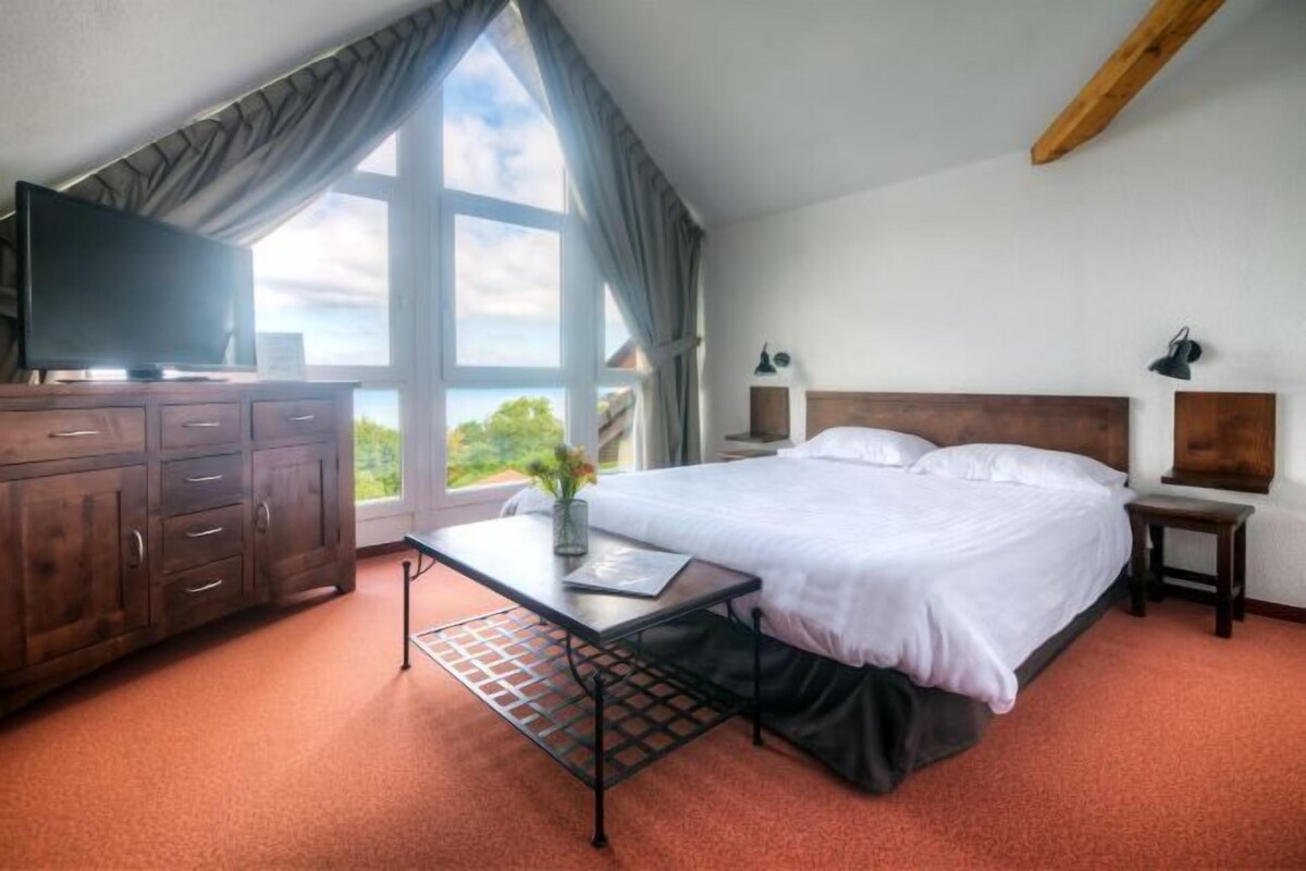 A bedroom with a bed, a desk, a TV, and a window with curtains.